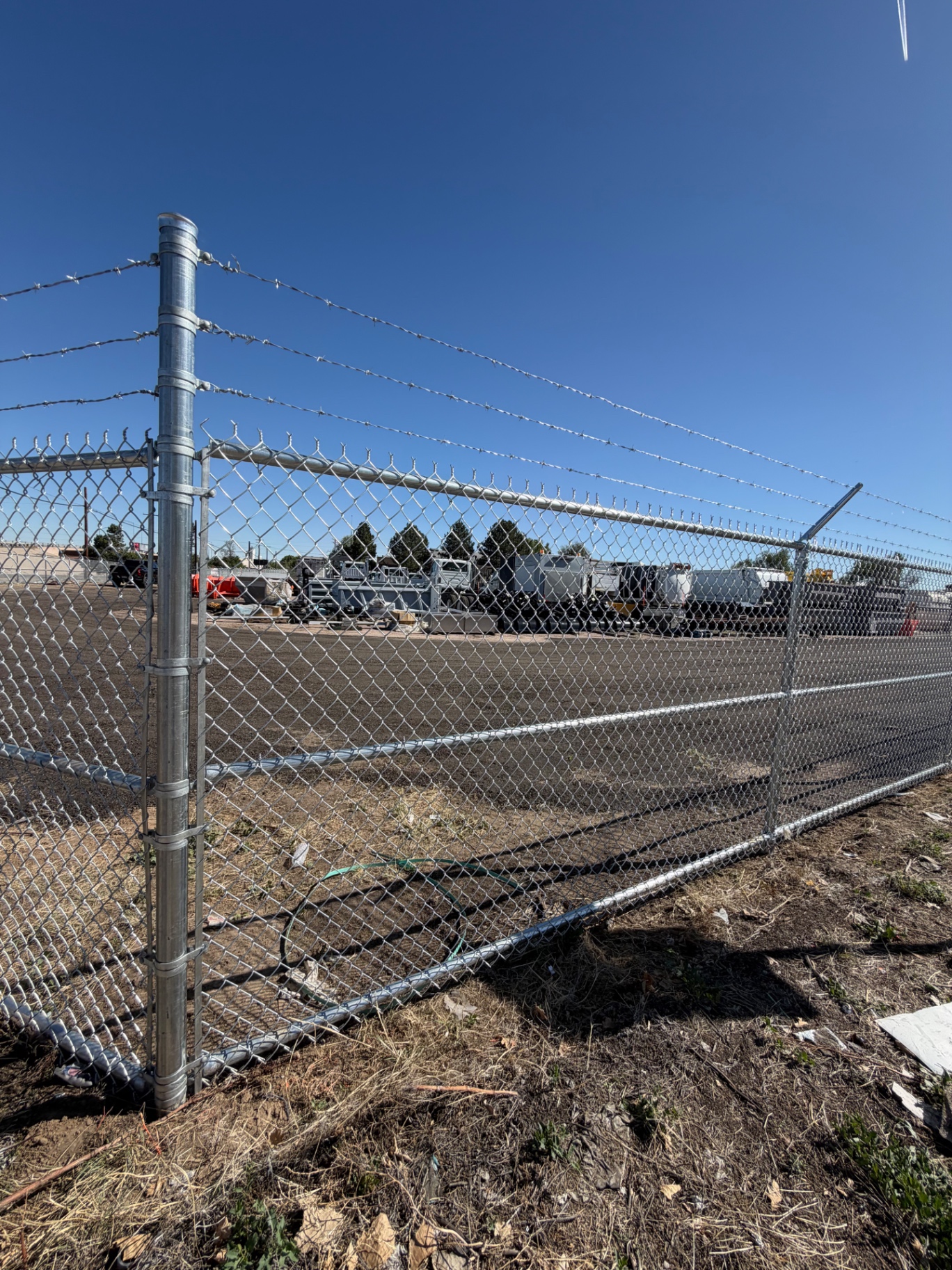 Close view of galvanized chain link security fence with barbed wire arms and corner post