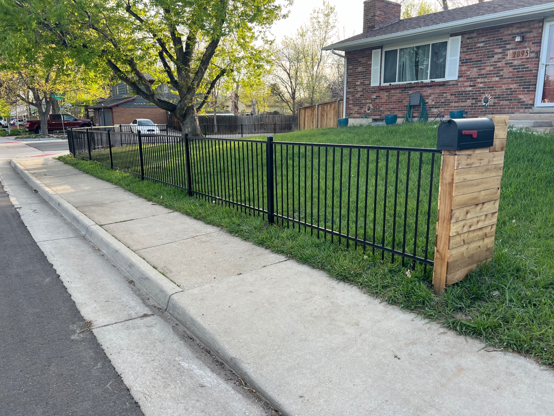 Black residential ornamental iron front yard fence installed along a residential sidewalk